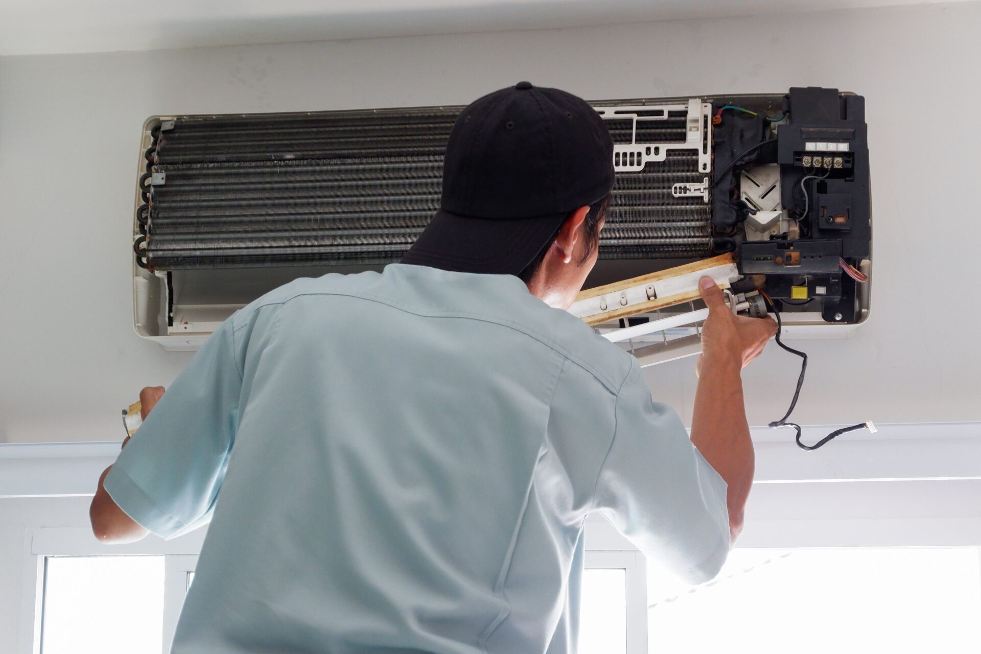 Technician repairing outdoor AC unit beside Alvin home during summer heat