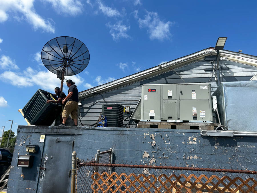 Technicians working on the roof of a building to install or maintain an air conditioning unit under a clear blue sky.