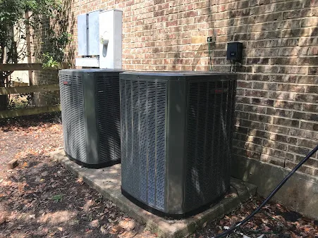 Two air conditioning condensers installed side by side against a brick home